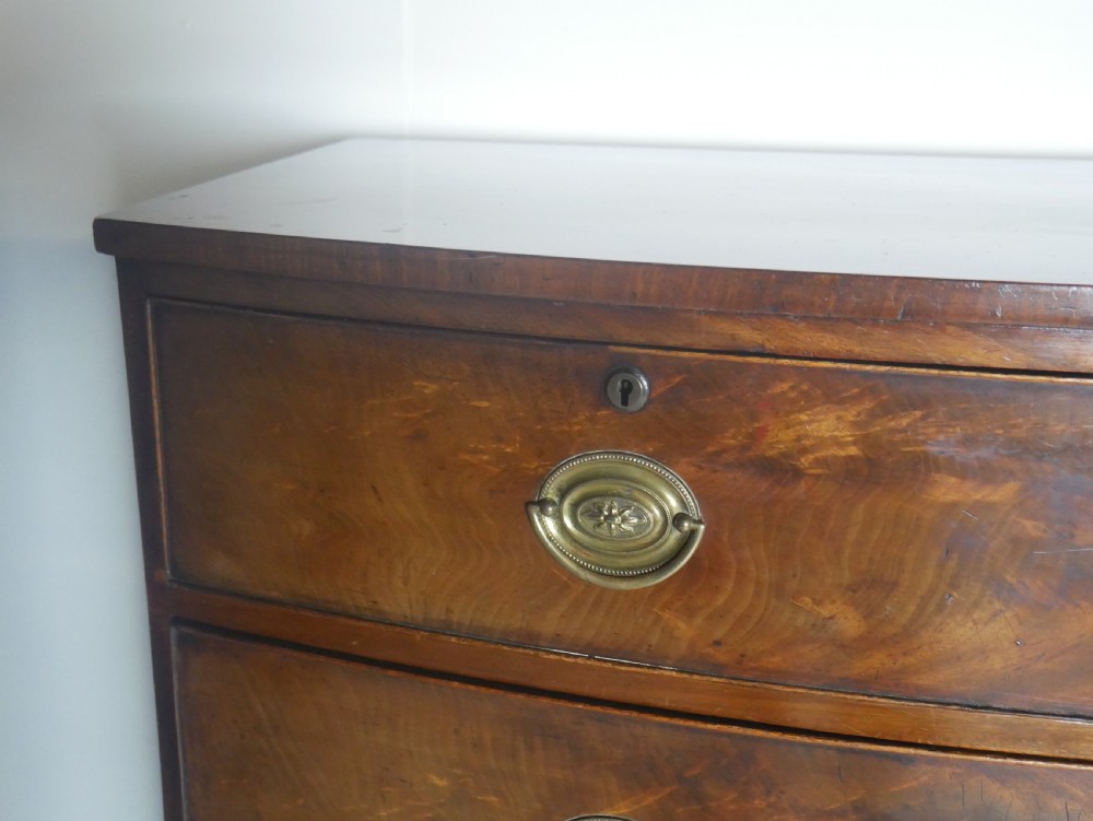 An early nineteenth-century mahogany bow-front chest of drawers featuring two short drawers over three long drawers with oval brass handles and splayed feet. View VII