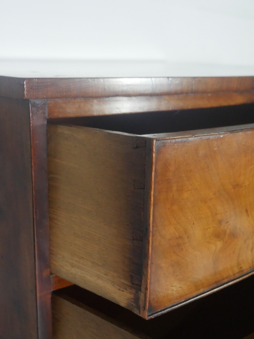 An early nineteenth-century mahogany bow-front chest of drawers featuring two short drawers over three long drawers with oval brass handles and splayed feet. View IX