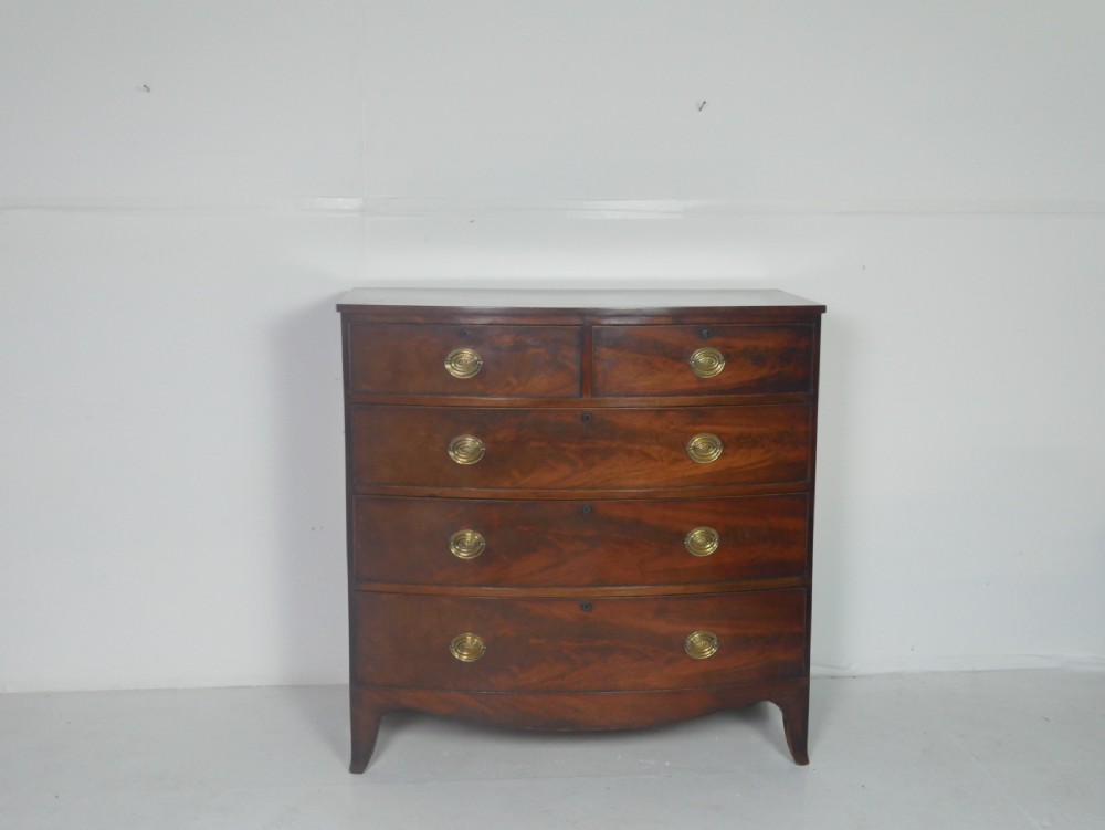 An early nineteenth-century mahogany bow-front chest of drawers featuring two short drawers over three long drawers with oval brass handles and splayed feet. View X