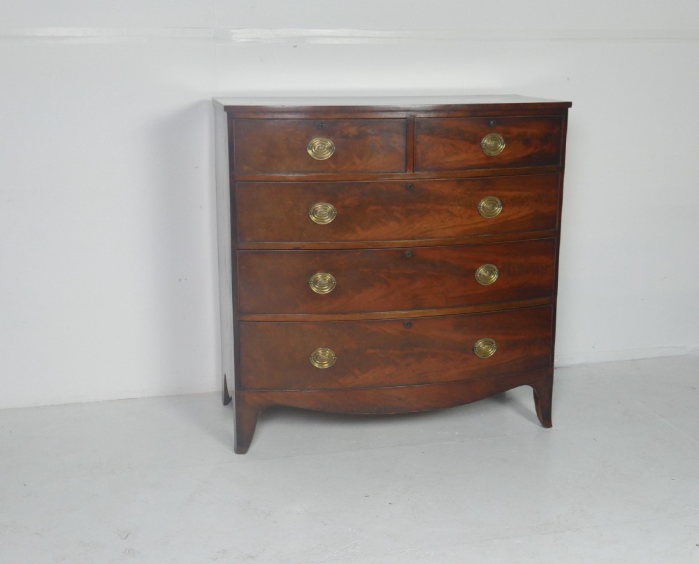 An early nineteenth-century mahogany bow-front chest of drawers featuring two short drawers over three long drawers with oval brass handles and splayed feet. View XI