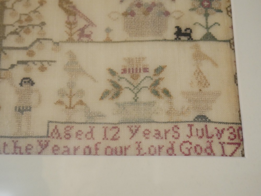 An 18th-century framed needlework sampler featuring a central brick house motif surrounded by trees, animals, figures, and stitched text on a linen ground. View V