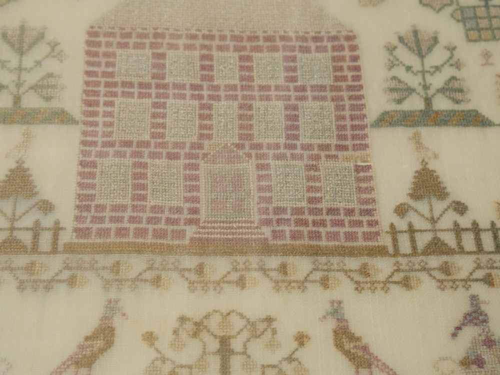 An 18th-century framed needlework sampler featuring a central brick house motif surrounded by trees, animals, figures, and stitched text on a linen ground. View VI