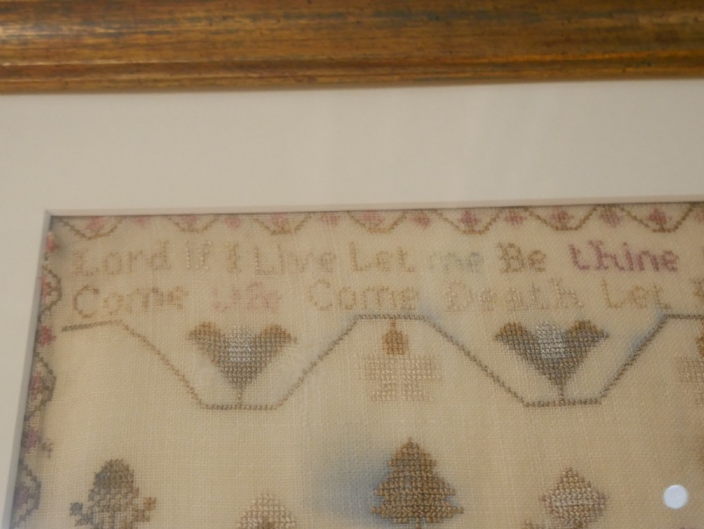 An 18th-century framed needlework sampler featuring a central brick house motif surrounded by trees, animals, figures, and stitched text on a linen ground. View VII