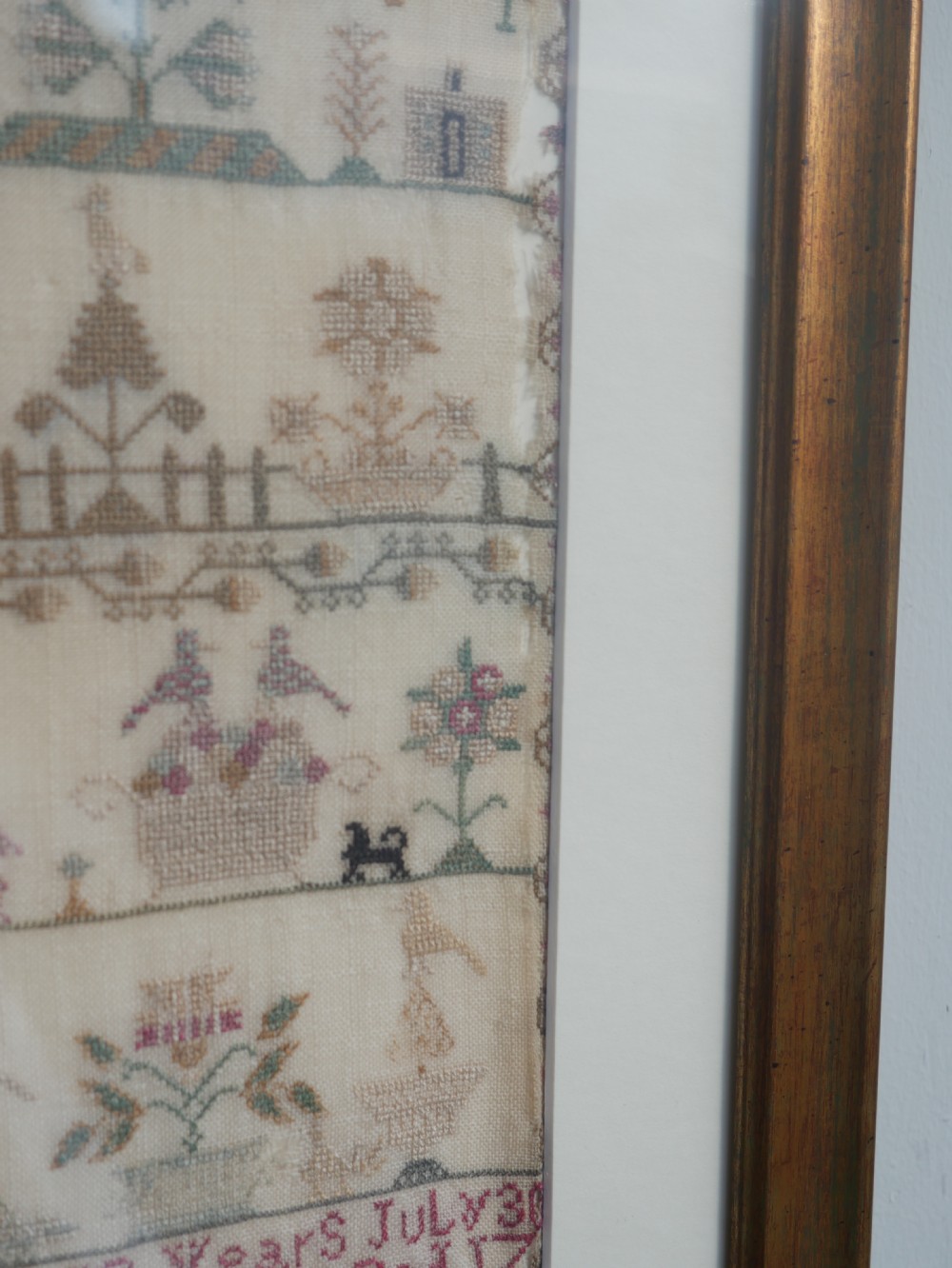 An 18th-century framed needlework sampler featuring a central brick house motif surrounded by trees, animals, figures, and stitched text on a linen ground. View XIII