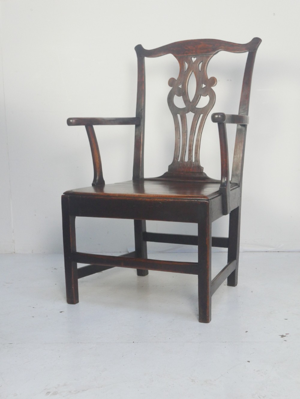 A dark wood Georgian country armchair featuring a pierced back splat with a heart motif, solid seat, curved armrests, and a sturdy stretcher base. View X