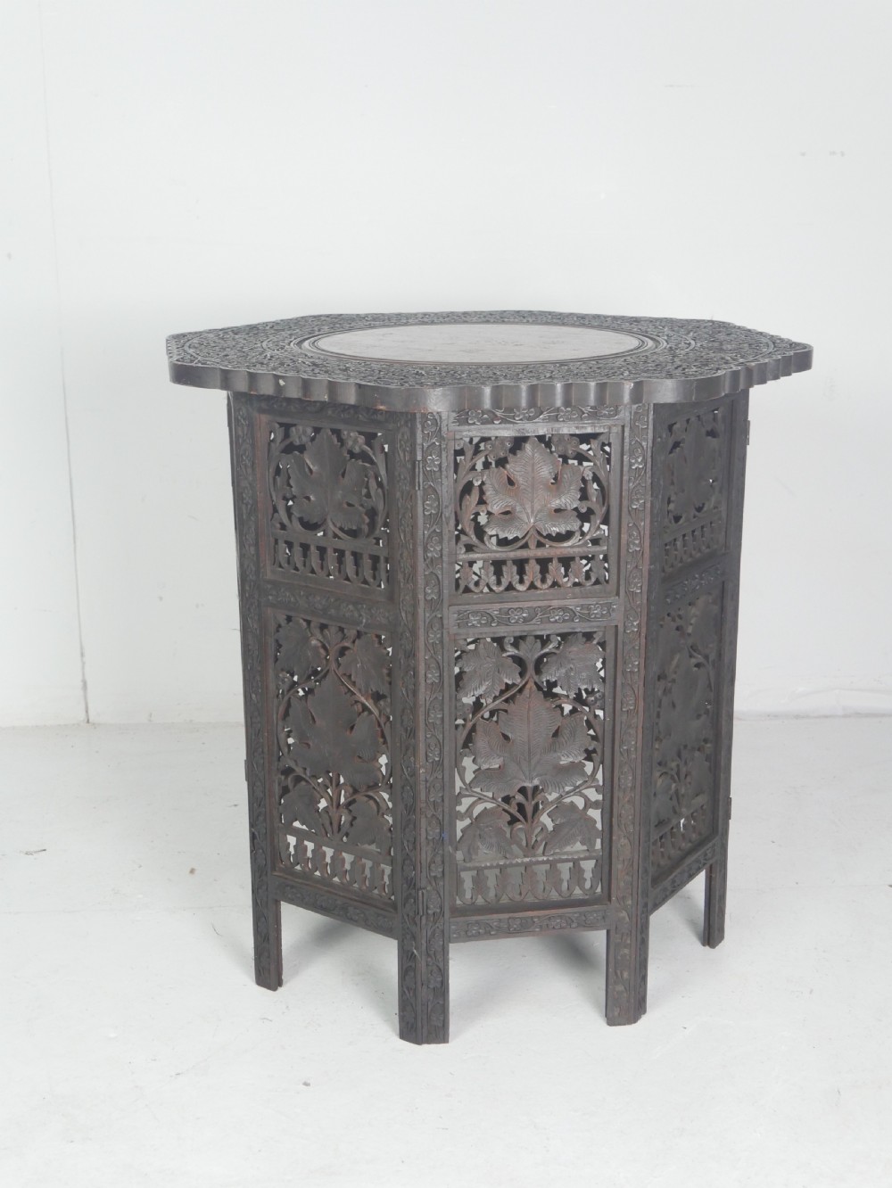 A dark hardwood octagonal side table featuring openwork fretwork panels carved with foliage motifs and a brass inlaid top surface.