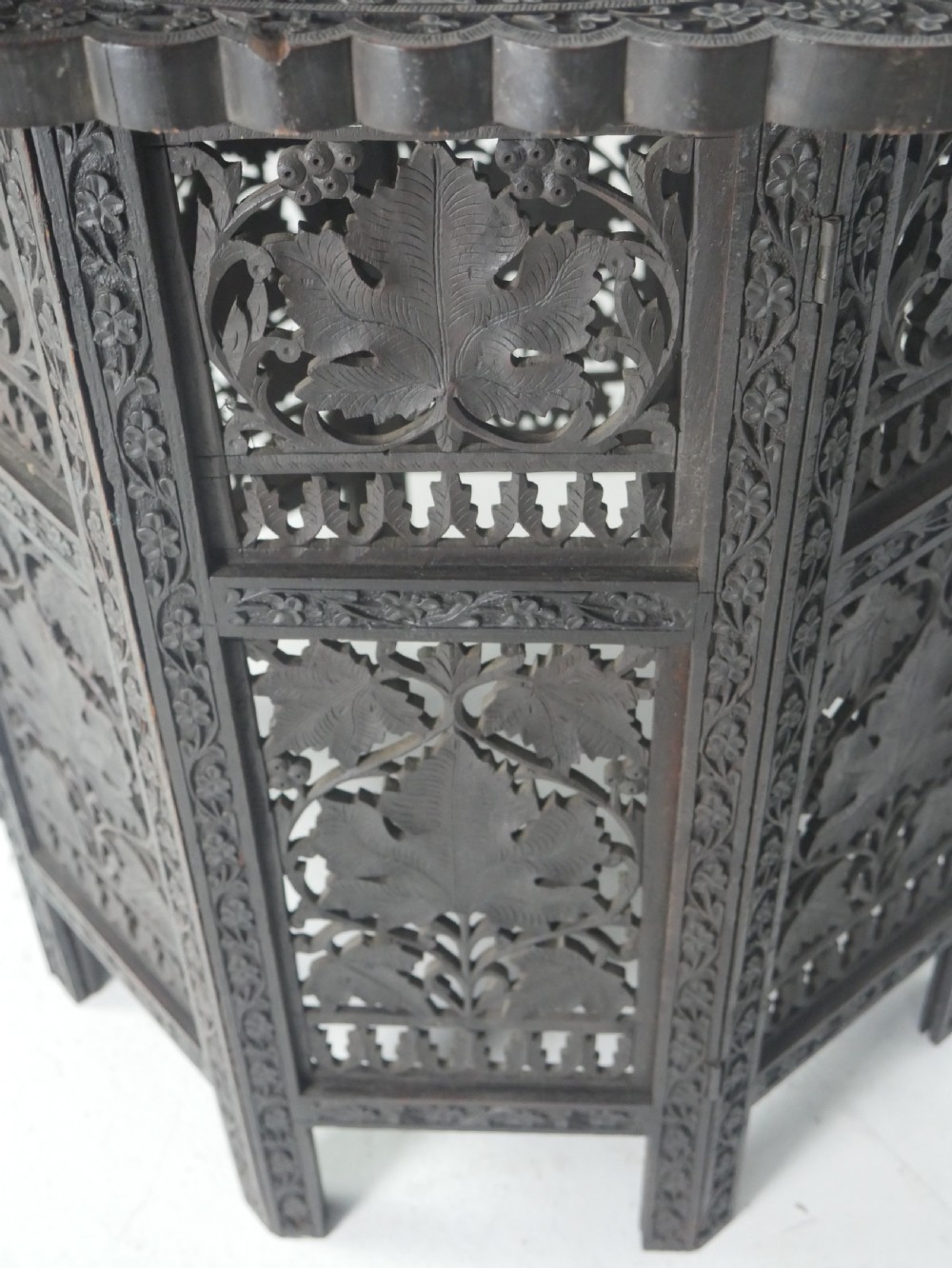 A dark hardwood octagonal side table featuring openwork fretwork panels carved with foliage motifs and a brass inlaid top surface. View VI