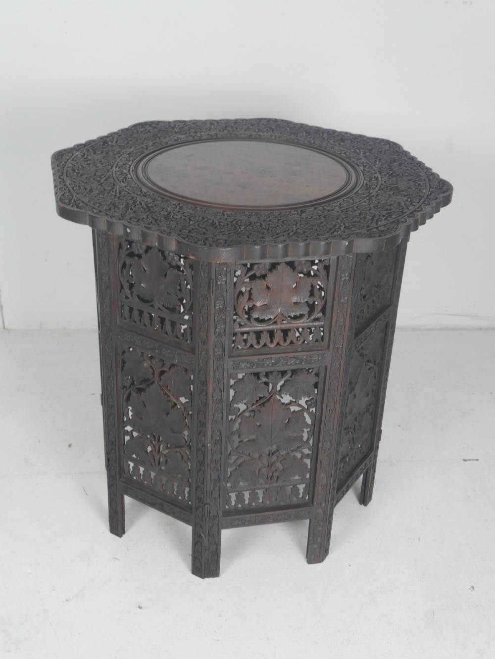 A dark hardwood octagonal side table featuring openwork fretwork panels carved with foliage motifs and a brass inlaid top surface. View IX