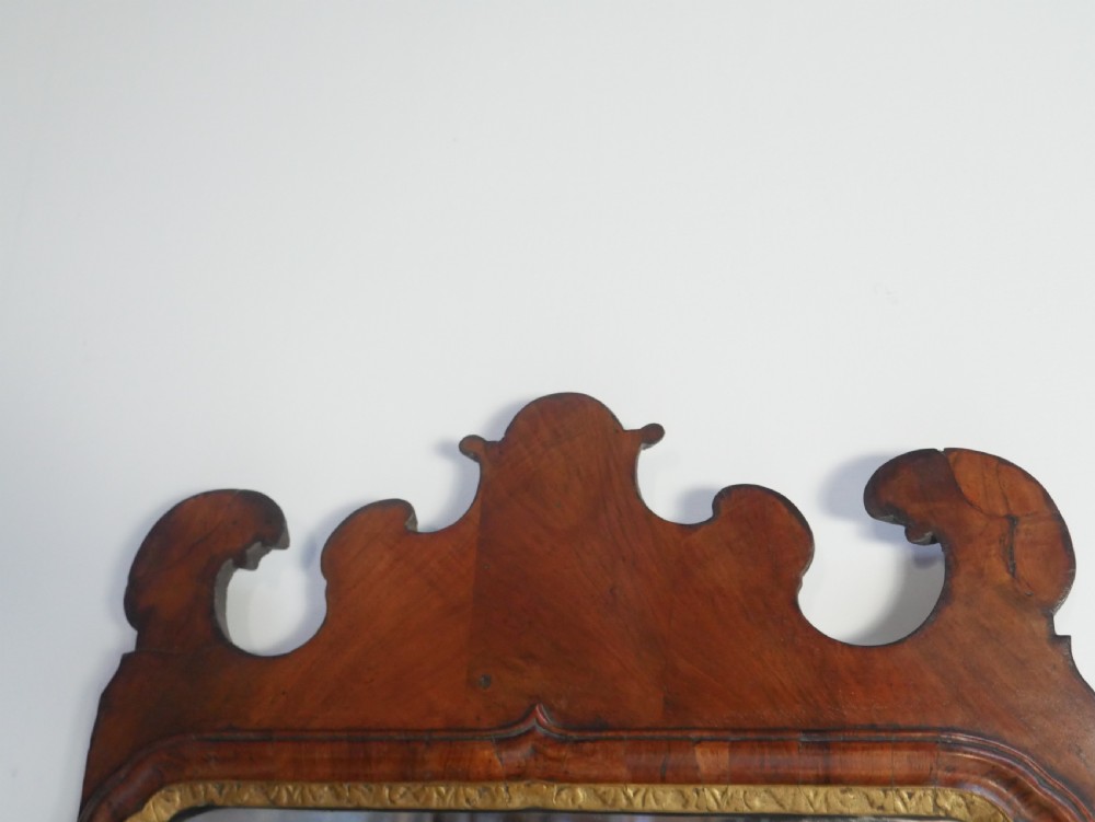 An 18th-century walnut wall mirror featuring a scroll-carved crest and apron, rounded upper corners, and a gilded inner moulding frame. View II