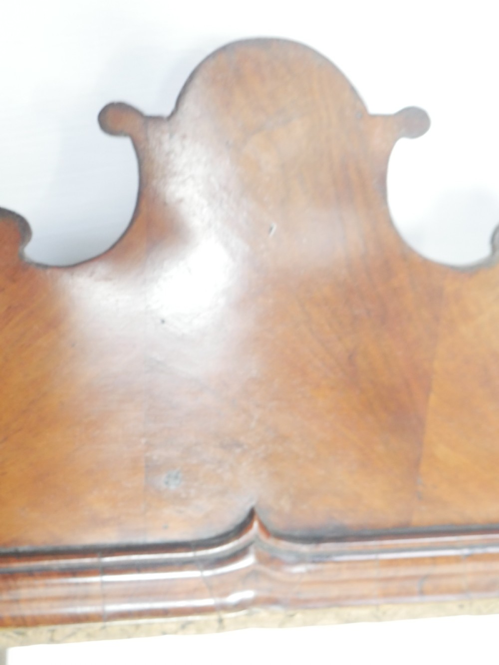 An 18th-century walnut wall mirror featuring a scroll-carved crest and apron, rounded upper corners, and a gilded inner moulding frame. View V