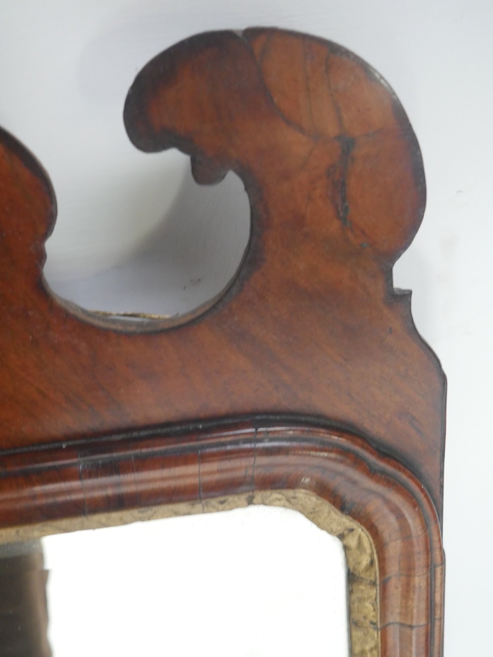 An 18th-century walnut wall mirror featuring a scroll-carved crest and apron, rounded upper corners, and a gilded inner moulding frame. View VI