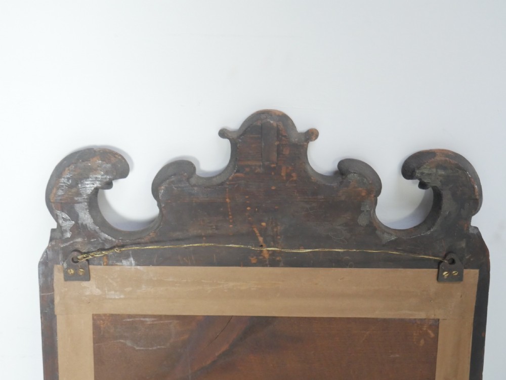 An 18th-century walnut wall mirror featuring a scroll-carved crest and apron, rounded upper corners, and a gilded inner moulding frame. View IX