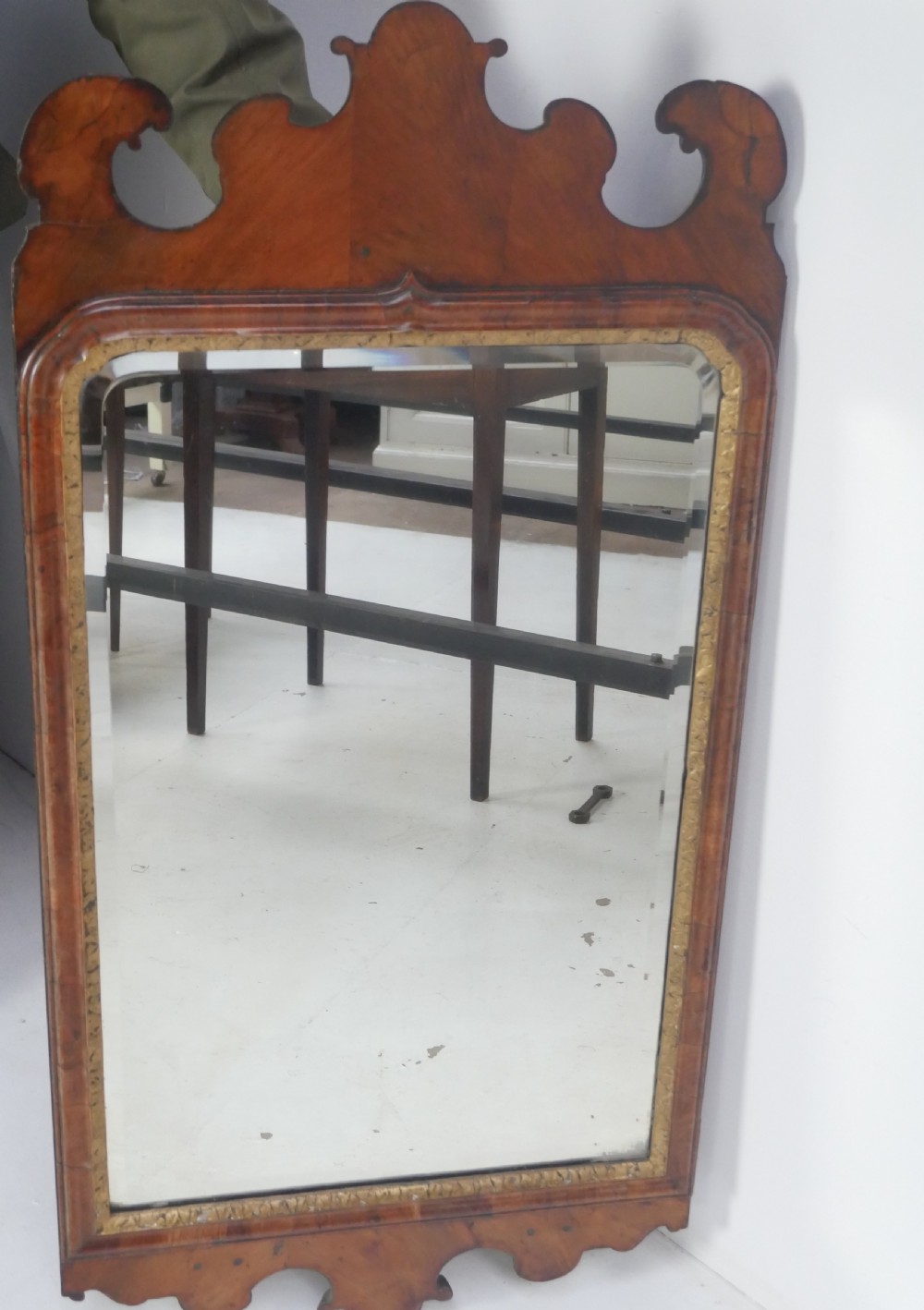An 18th-century walnut wall mirror featuring a scroll-carved crest and apron, rounded upper corners, and a gilded inner moulding frame. View X