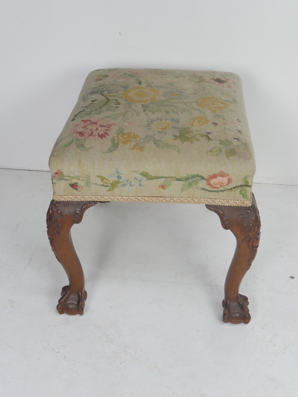 A square upholstered footstool featuring floral needlepoint fabric, carved cabriole legs, and claw and ball feet. View II