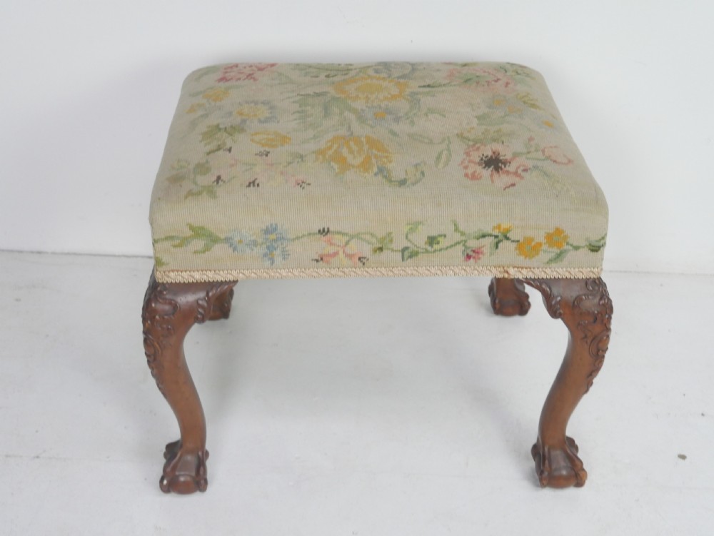 A square upholstered footstool featuring floral needlepoint fabric, carved cabriole legs, and claw and ball feet. View V