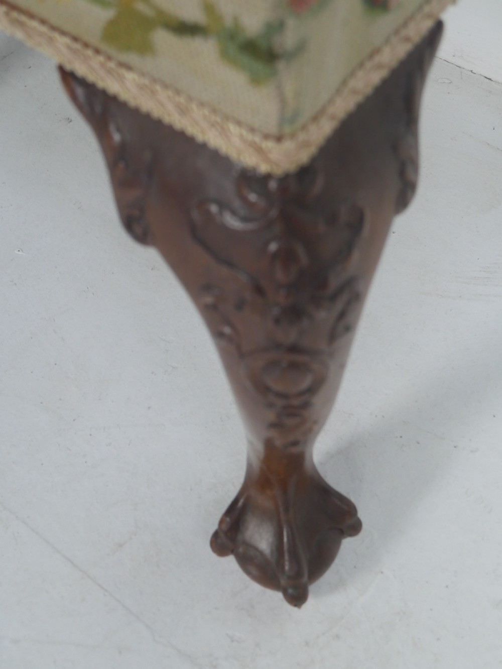 A square upholstered footstool featuring floral needlepoint fabric, carved cabriole legs, and claw and ball feet. View VII