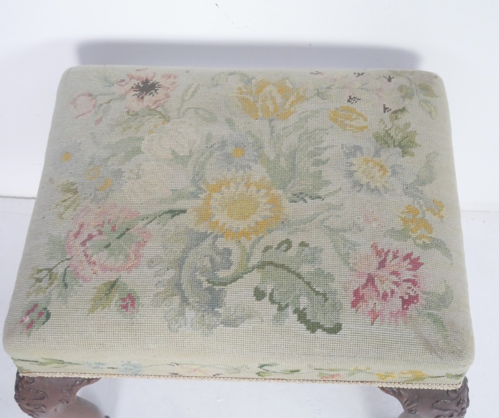 A square upholstered footstool featuring floral needlepoint fabric, carved cabriole legs, and claw and ball feet. View VIII