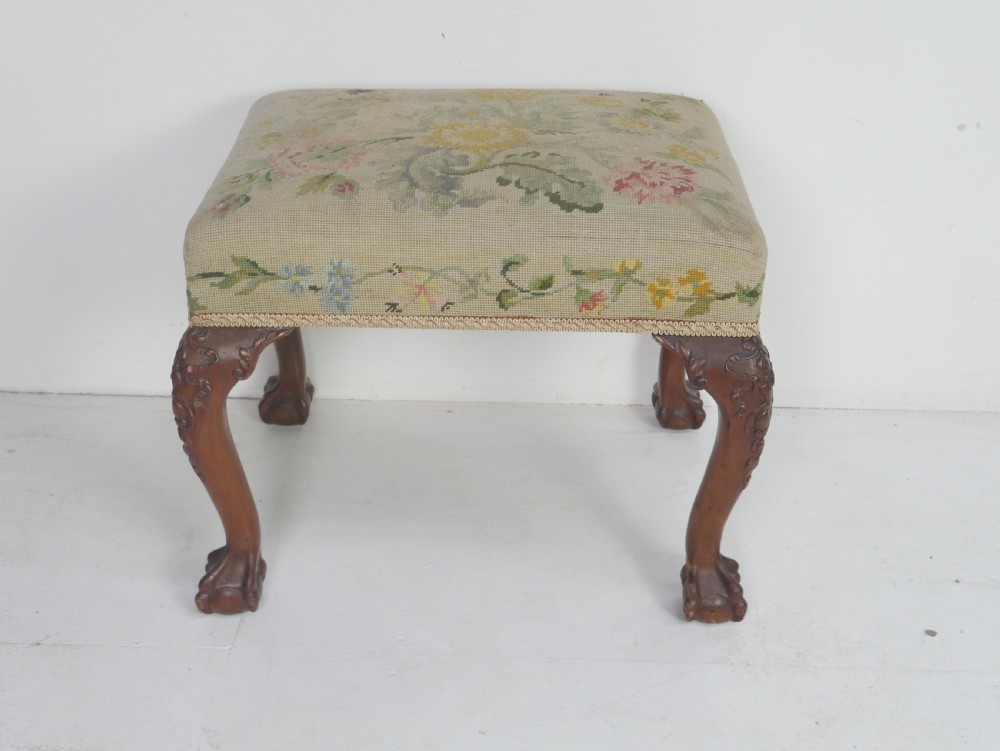 A square upholstered footstool featuring floral needlepoint fabric, carved cabriole legs, and claw and ball feet. View X