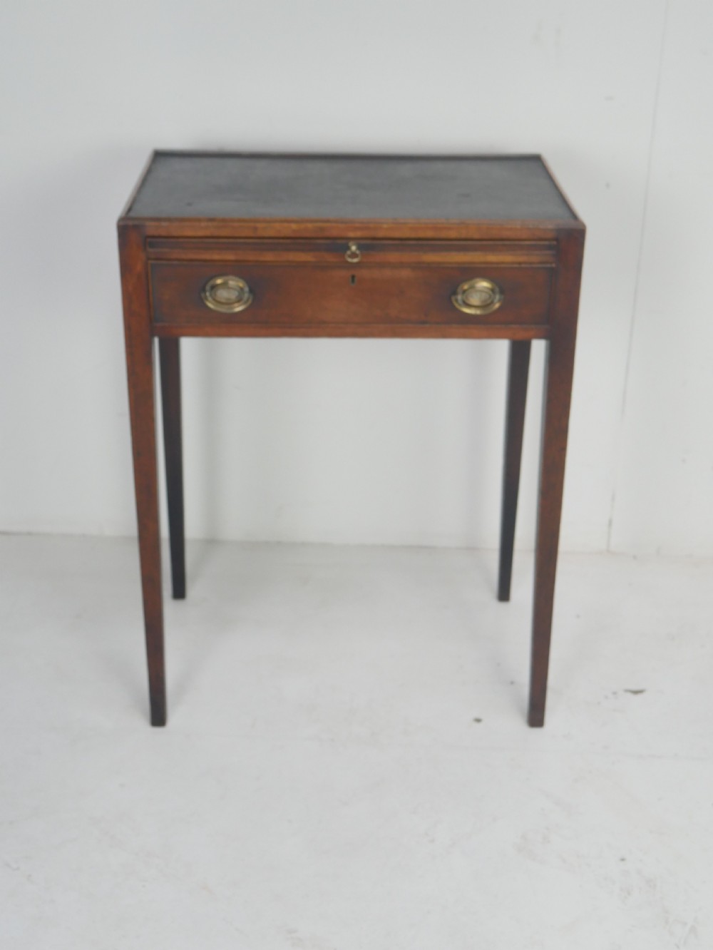 A Georgian mahogany side table featuring a dark leather inset top, frieze drawer with brass handles, and slender tapered legs.