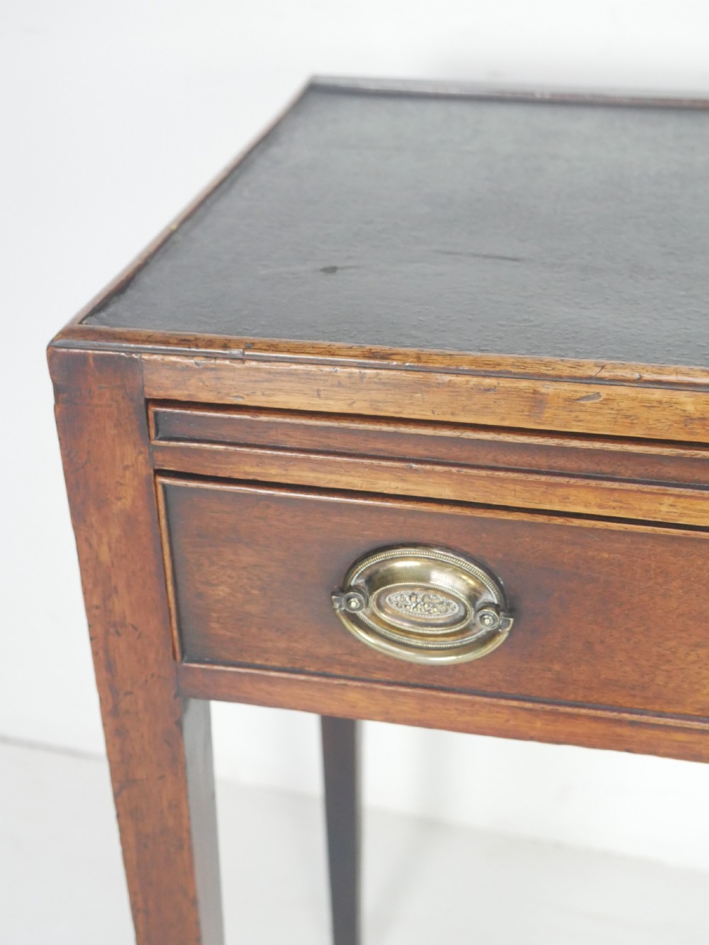 A Georgian mahogany side table featuring a dark leather inset top, frieze drawer with brass handles, and slender tapered legs. View V