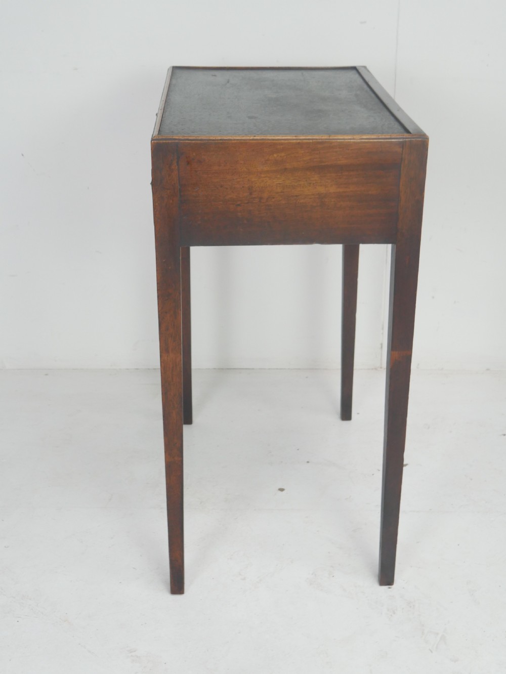 A Georgian mahogany side table featuring a dark leather inset top, frieze drawer with brass handles, and slender tapered legs. View X