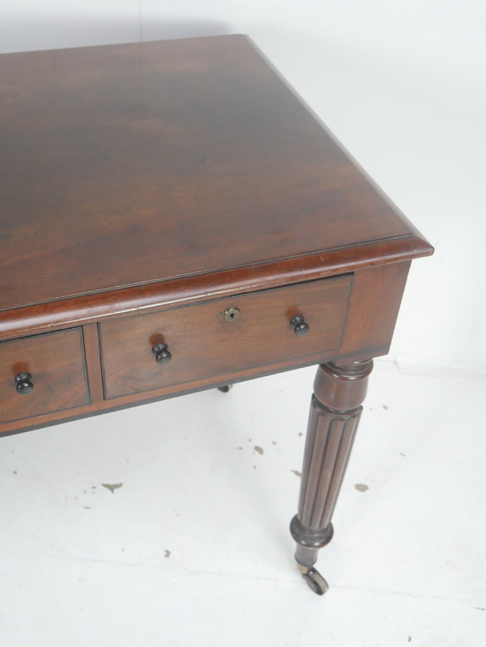 An English Regency mahogany freestanding writing desk featuring three frieze drawers with small turned knobs, supported by four reeded legs on brass castors. View III