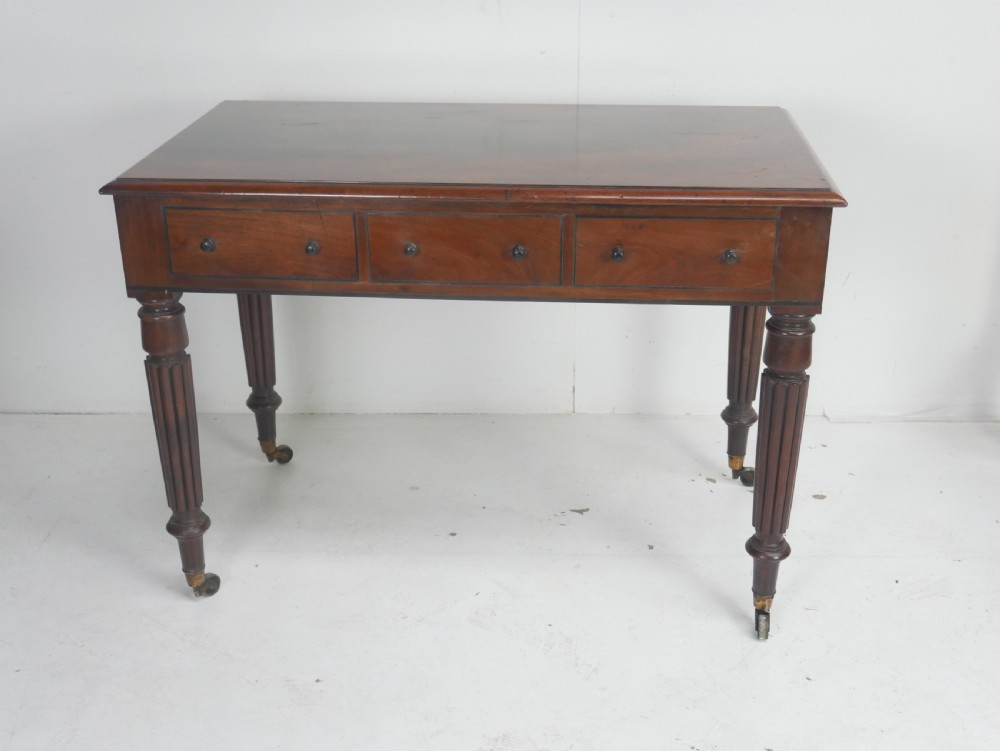 An English Regency mahogany freestanding writing desk featuring three frieze drawers with small turned knobs, supported by four reeded legs on brass castors. View IX