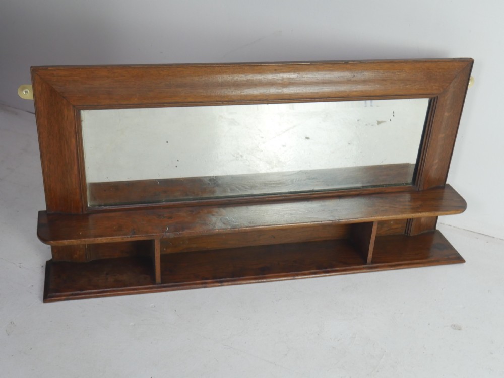 A rectangular antique oak hall mirror featuring a moulded wooden frame, central reflective glass, and an integrated lower display shelf with small cubby compartments.