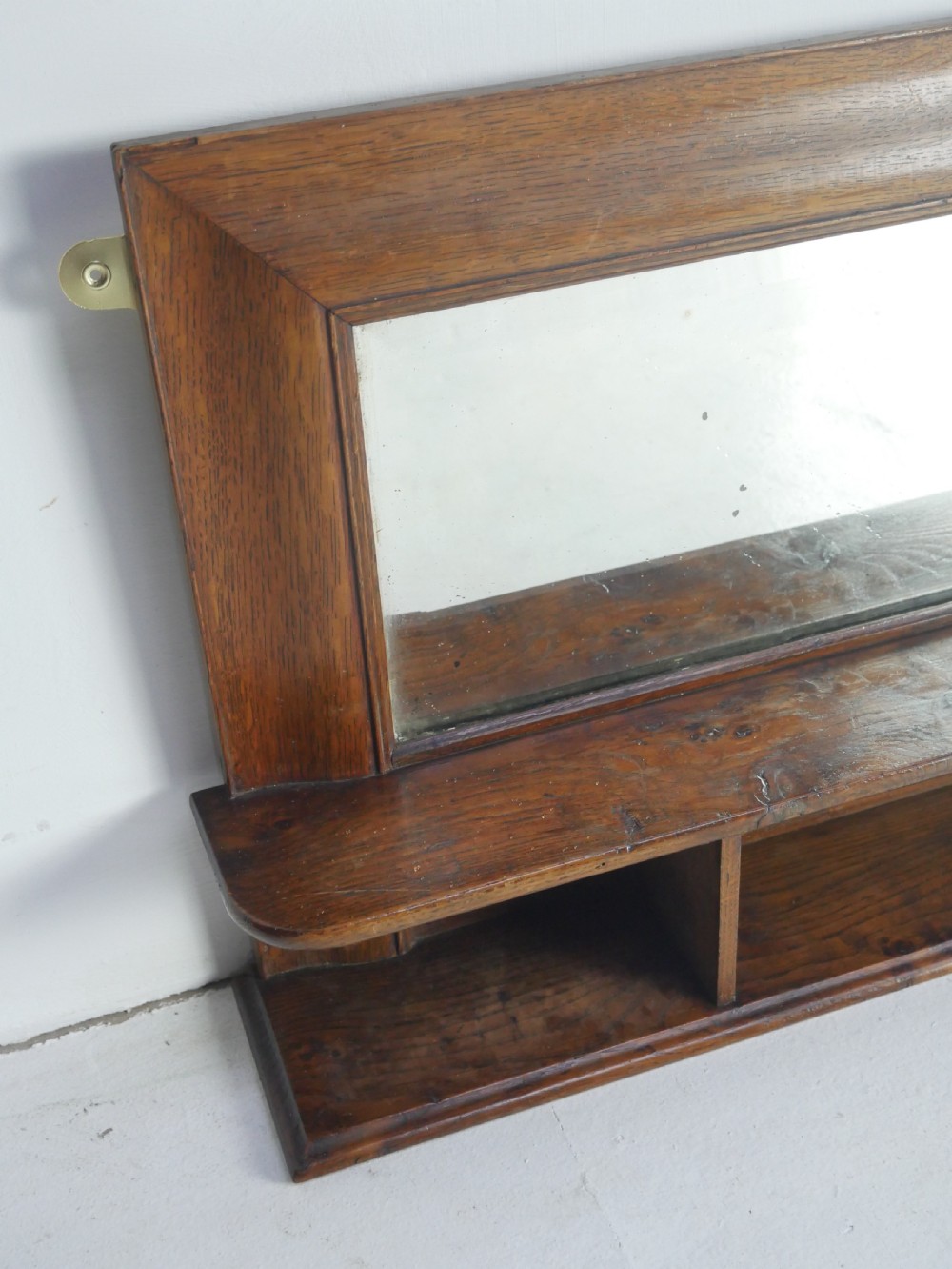 A rectangular antique oak hall mirror featuring a moulded wooden frame, central reflective glass, and an integrated lower display shelf with small cubby compartments. View III
