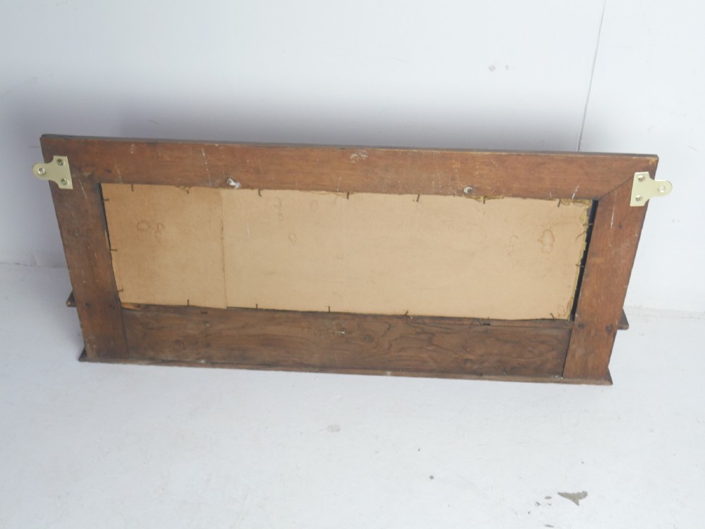 A rectangular antique oak hall mirror featuring a moulded wooden frame, central reflective glass, and an integrated lower display shelf with small cubby compartments. View VI