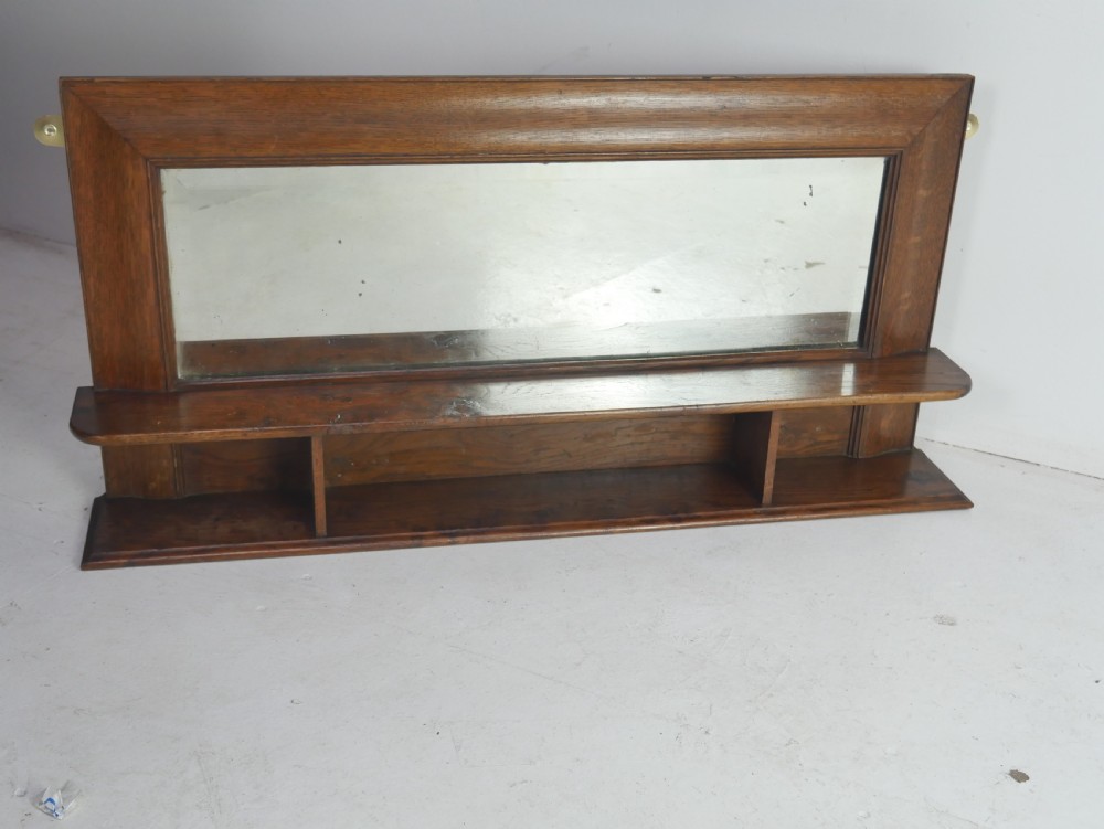 A rectangular antique oak hall mirror featuring a moulded wooden frame, central reflective glass, and an integrated lower display shelf with small cubby compartments. View VII