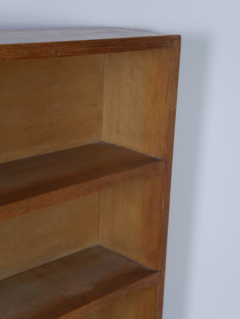 A wide wooden open bookcase made of light oak with four horizontal shelves and a simple plinth base. View VII