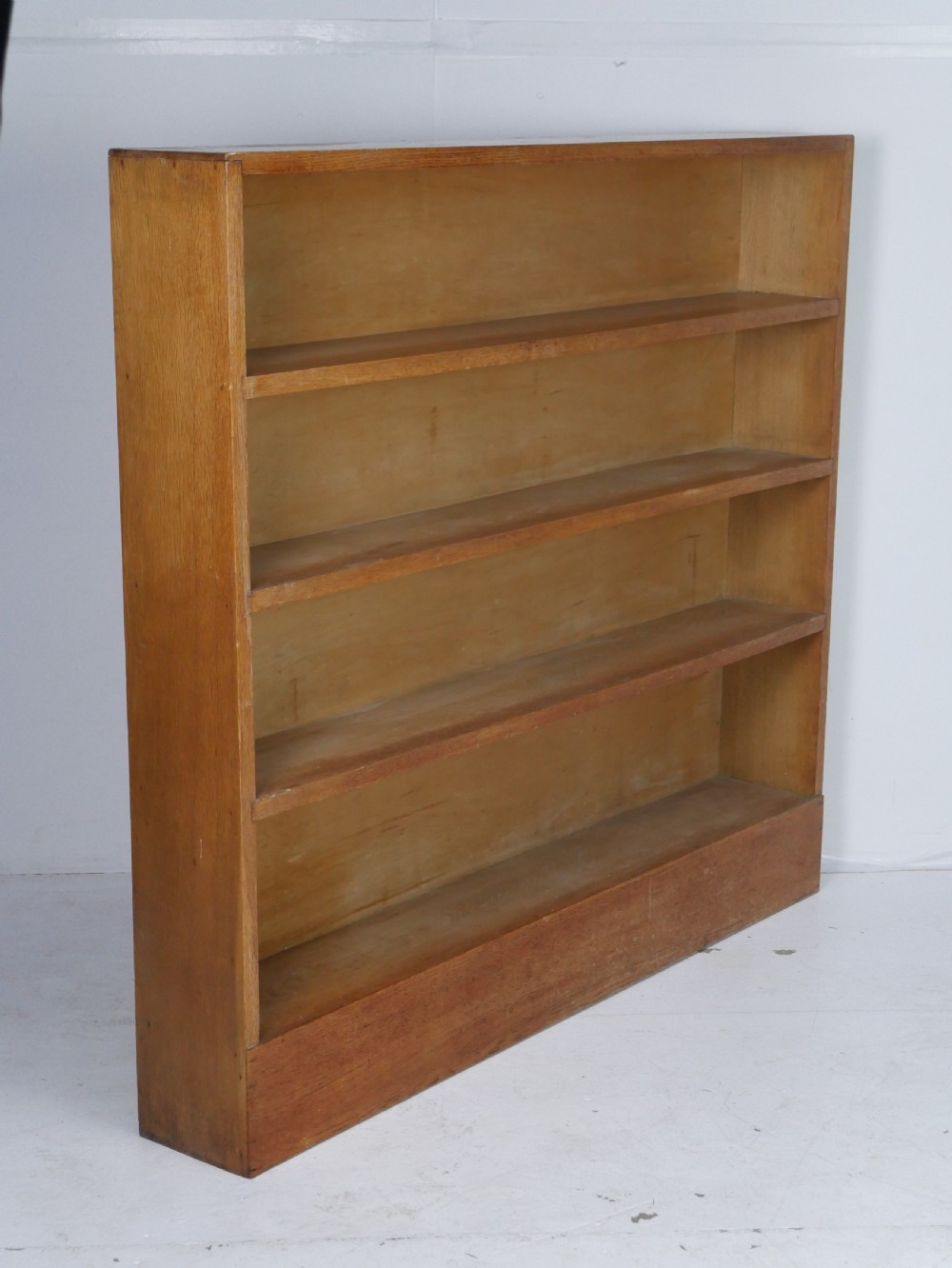 A wide wooden open bookcase made of light oak with four horizontal shelves and a simple plinth base. View X