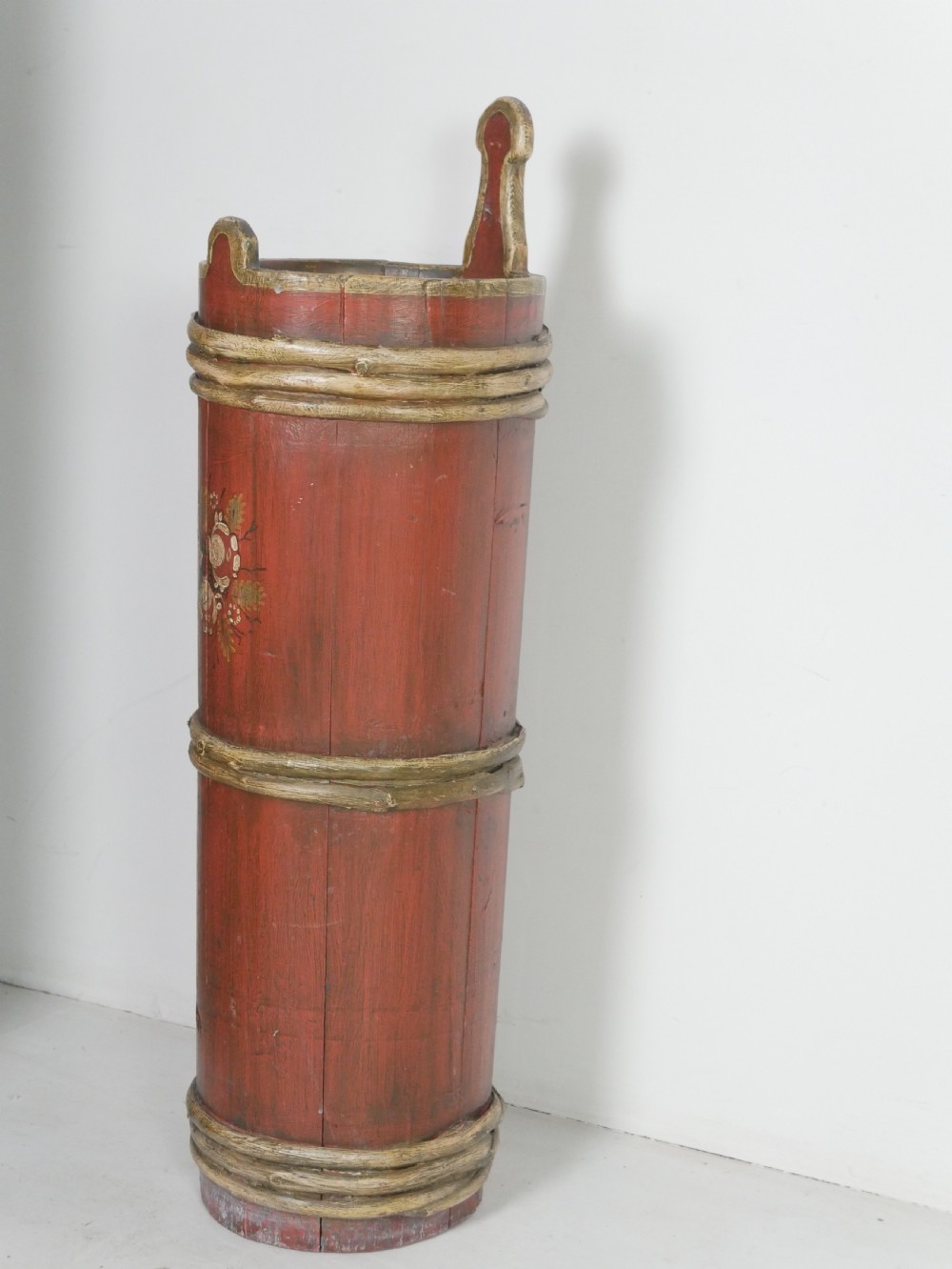 A tall, cylindrical red-painted wooden umbrella stand featuring hand-painted floral motifs and raised wooden banding. View VIII