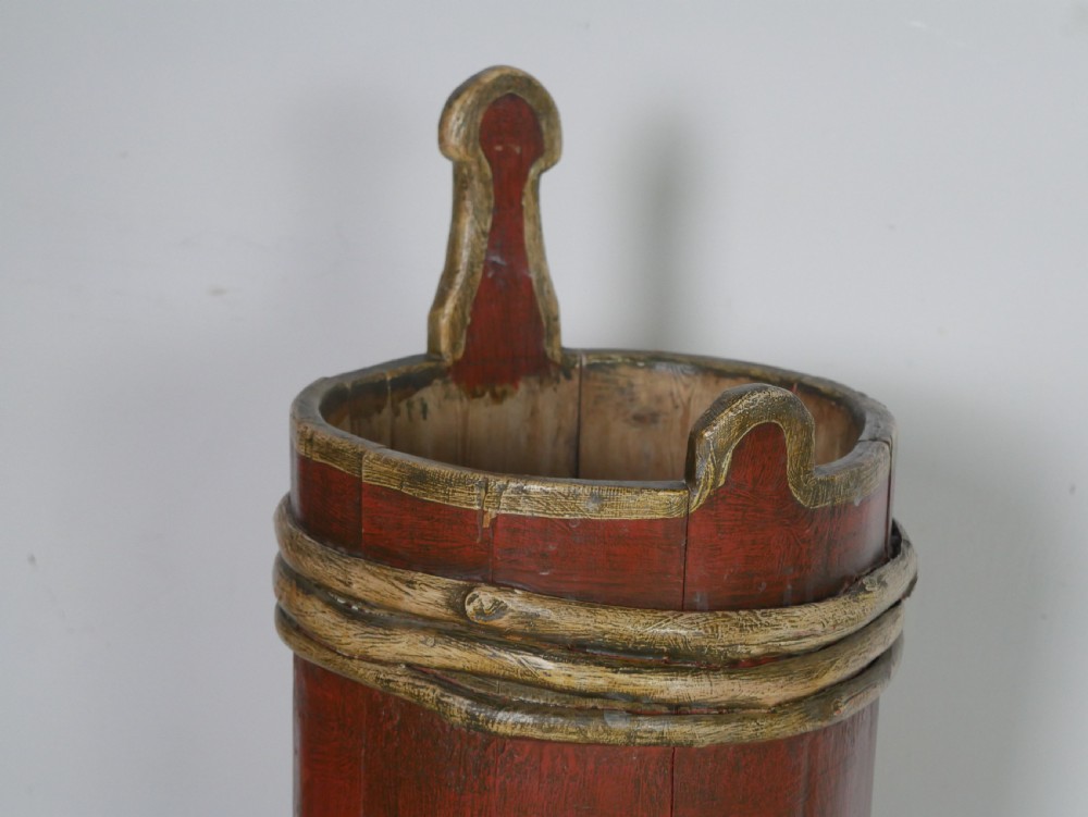 A tall, cylindrical red-painted wooden umbrella stand featuring hand-painted floral motifs and raised wooden banding. View IX