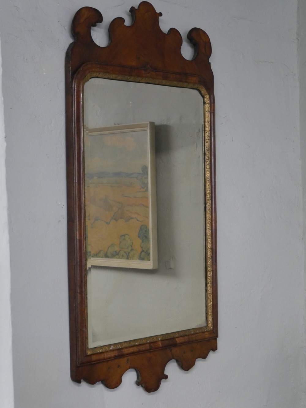 An 18th-century walnut wall mirror featuring a scroll-carved crest and apron, rounded upper corners, and a gilded inner moulding frame.
