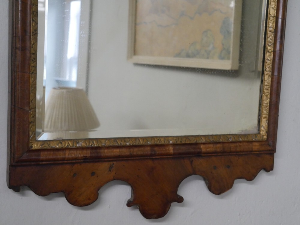 An 18th-century walnut wall mirror featuring a scroll-carved crest and apron, rounded upper corners, and a gilded inner moulding frame. View XII