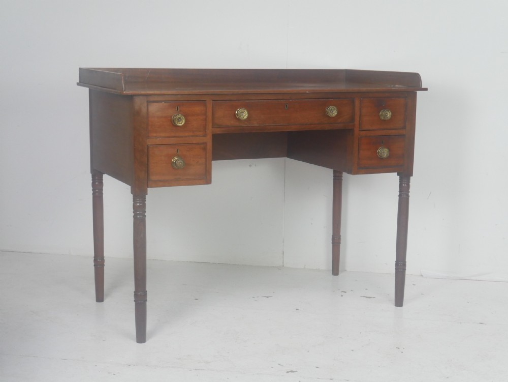 A Regency period mahogany writing desk featuring a low rear gallery, five drawers with brass handles, and four turned legs.