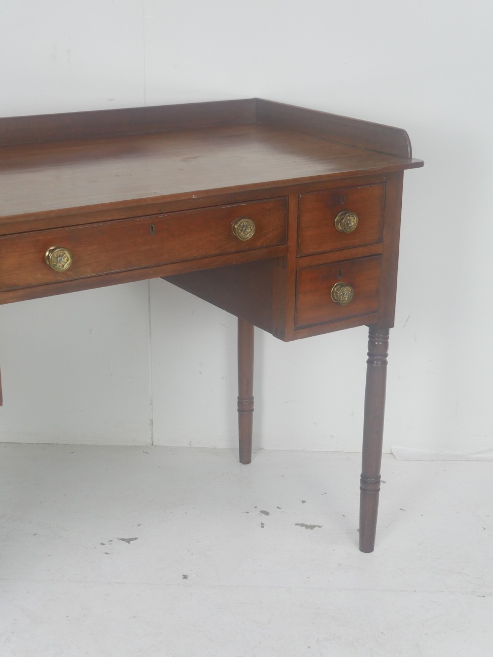 A Regency period mahogany writing desk featuring a low rear gallery, five drawers with brass handles, and four turned legs. View III