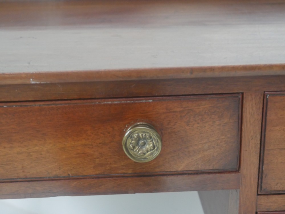 A Regency period mahogany writing desk featuring a low rear gallery, five drawers with brass handles, and four turned legs. View V