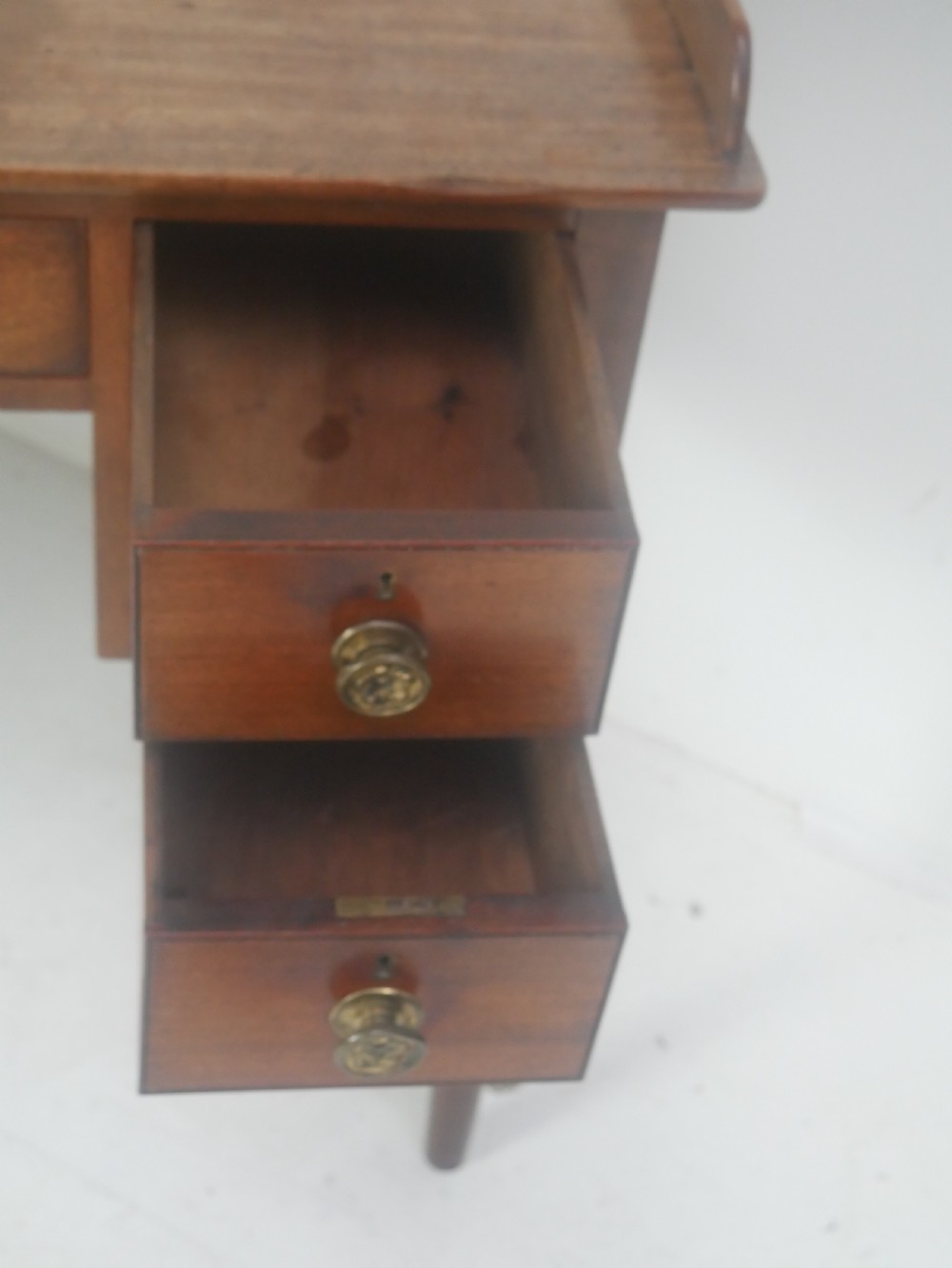A Regency period mahogany writing desk featuring a low rear gallery, five drawers with brass handles, and four turned legs. View VI