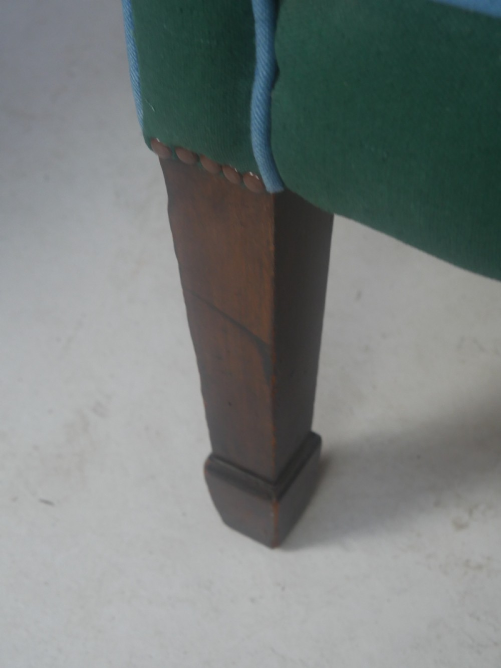 A forest green upholstered barrel back armchair with vertical channel tufting, light blue contrast piping, and dark tapered square legs. View II