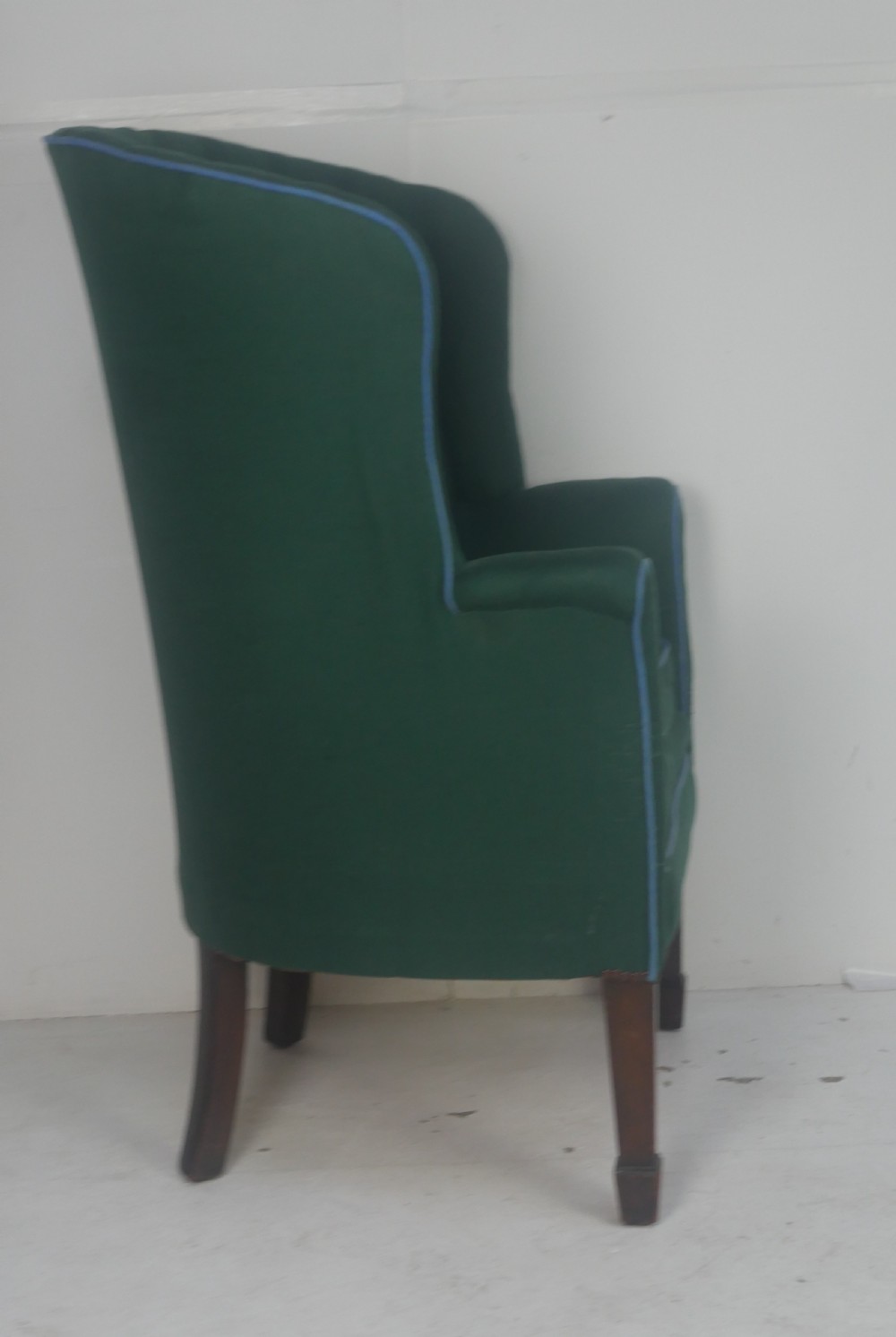 A forest green upholstered barrel back armchair with vertical channel tufting, light blue contrast piping, and dark tapered square legs. View V