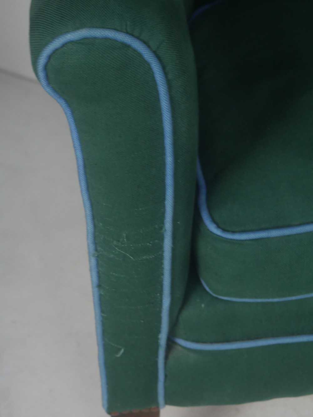 A forest green upholstered barrel back armchair with vertical channel tufting, light blue contrast piping, and dark tapered square legs. View X