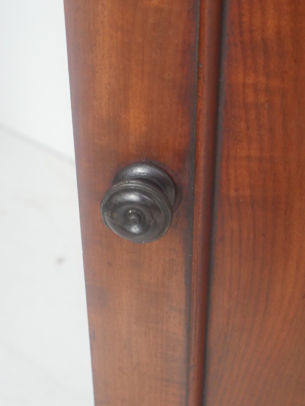 A 19th-century mahogany bedside cupboard featuring a single arched panel door, turned wooden knob, top galley edge, and a solid plinth base. View VII