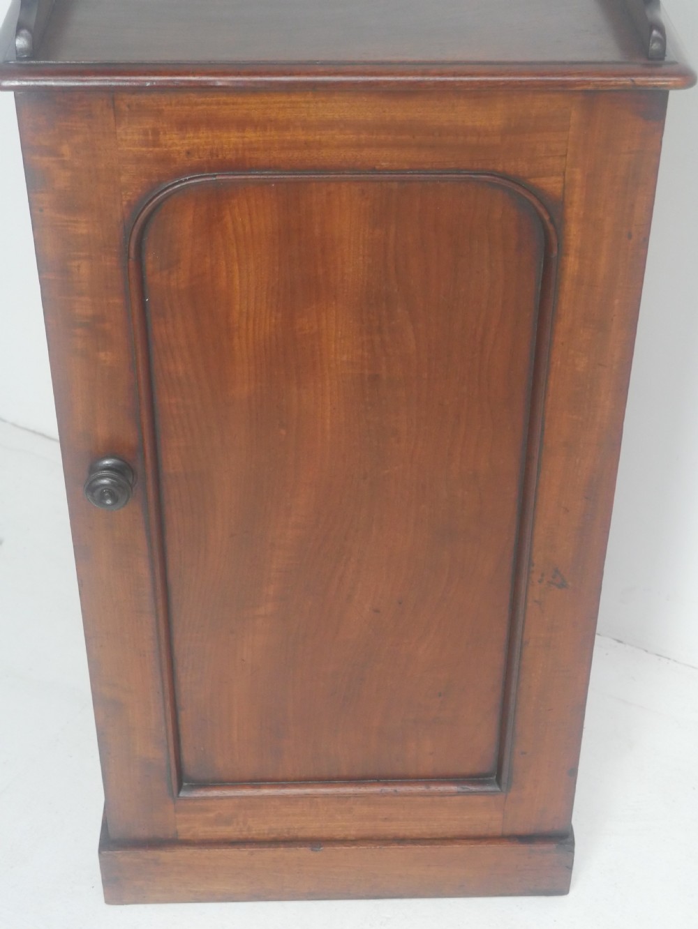 A 19th-century mahogany bedside cupboard featuring a single arched panel door, turned wooden knob, top galley edge, and a solid plinth base. View IX