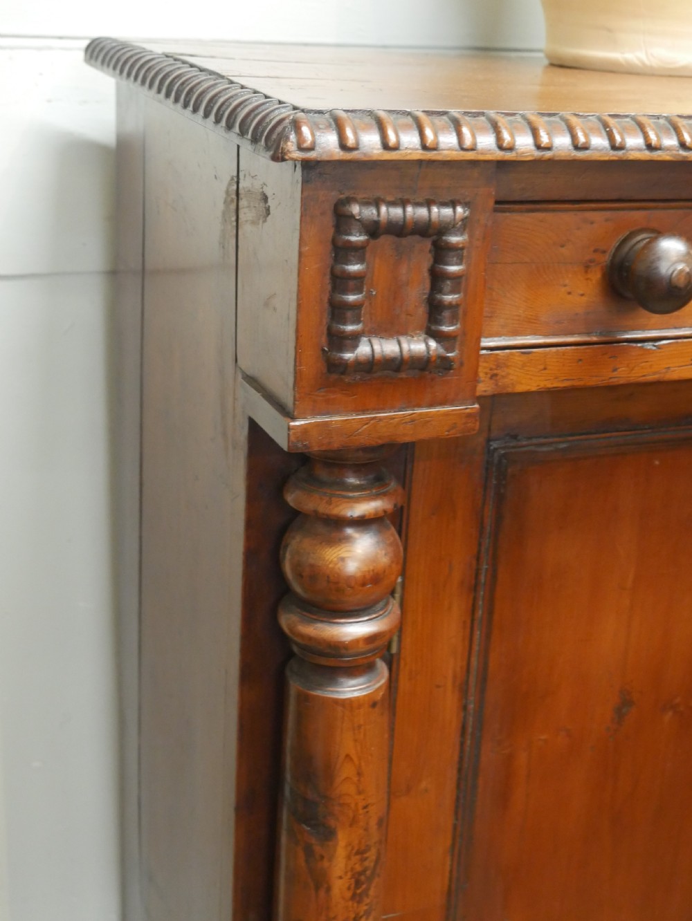 A warm brown cedar cupboard featuring two top drawers, twin panelled doors, and carved side columns supported by turned feet. View II