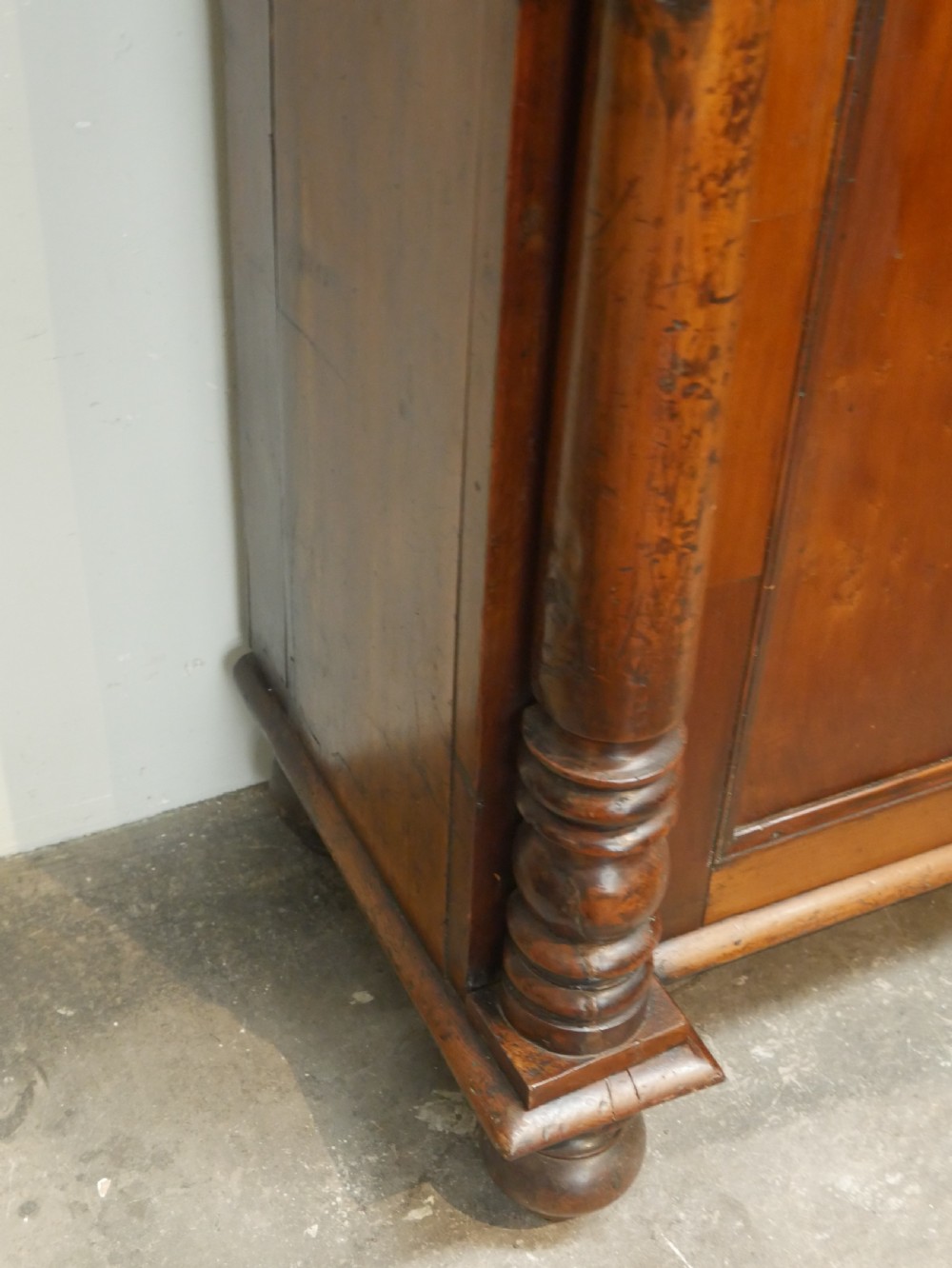 A warm brown cedar cupboard featuring two top drawers, twin panelled doors, and carved side columns supported by turned feet. View III