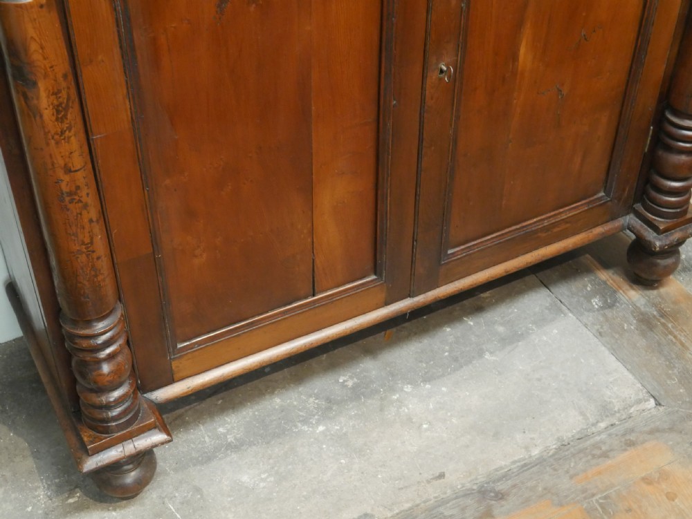 A warm brown cedar cupboard featuring two top drawers, twin panelled doors, and carved side columns supported by turned feet. View V