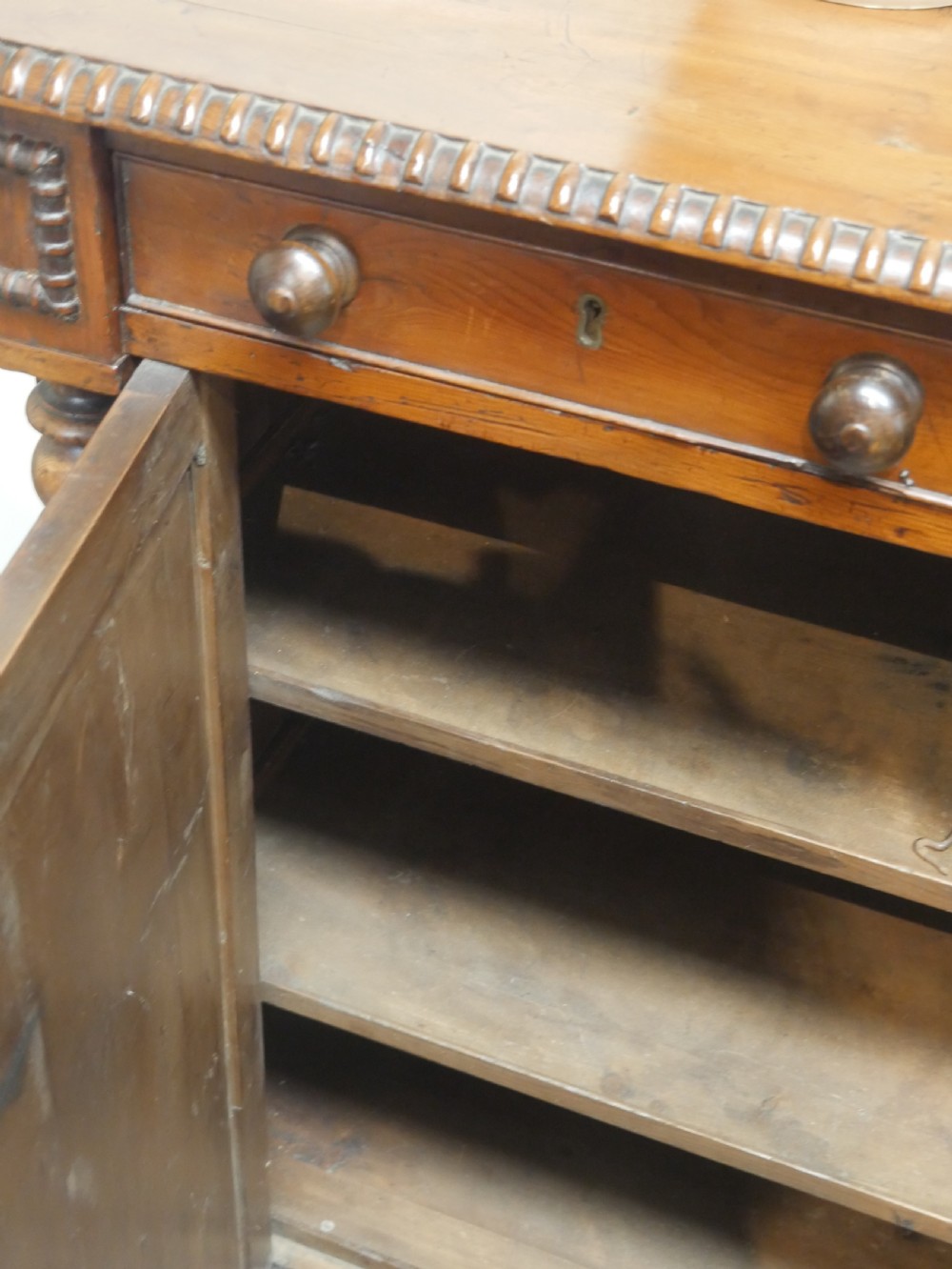 A warm brown cedar cupboard featuring two top drawers, twin panelled doors, and carved side columns supported by turned feet. View VII